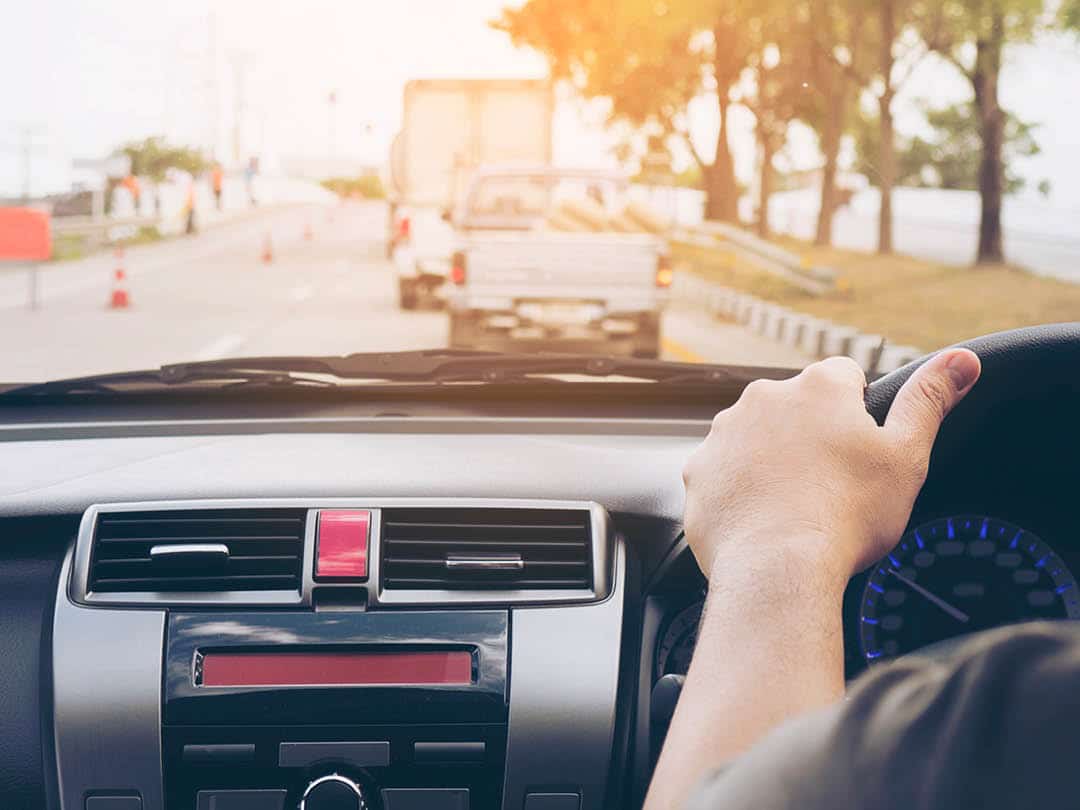 Person holding steering wheel looking into the sun