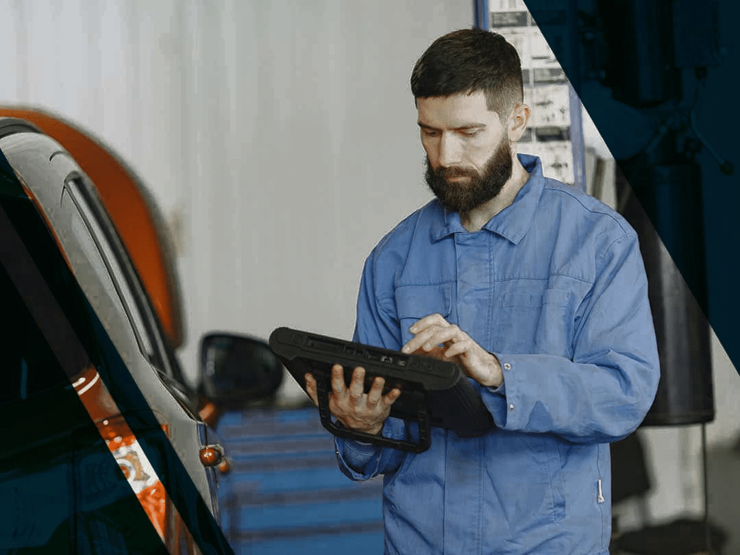 A-man-in-blue-coveralls A man in blue coveralls standing beside an orange car carrying out engine diagnostics