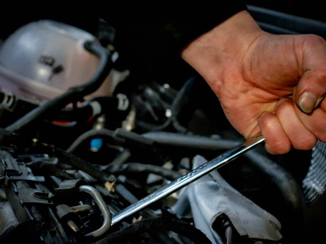 Mechanic tightening a bolt inside a car engine bay.